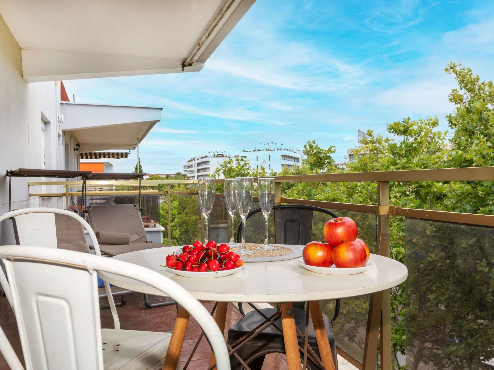 Een balkon met een tafel gedekt voor twee personen, met een bord kersen en appels, en twee lege wijnglazen.