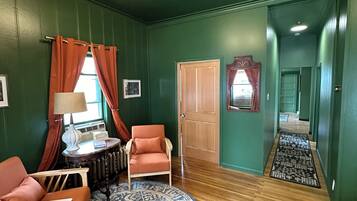 A room with green walls, a wooden floor, a round blue and white rug, two orange chairs, a table with a lamp, and a ceiling fan.