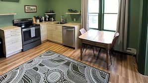 Une cuisine compacte comprenant une cuisinière, un évier et des placards, une table à manger avec des chaises, et un tapis à motifs.