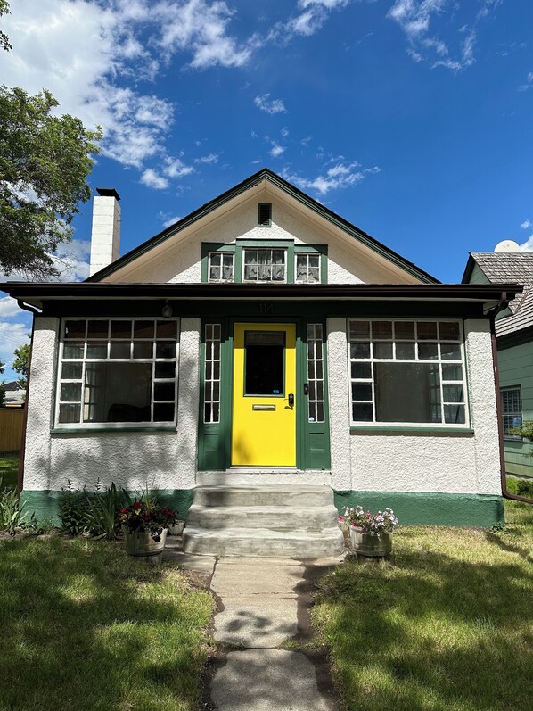 Una casa de dos pisos con puerta y ventanas verdes, una chimenea y el número 114 en la fachada.