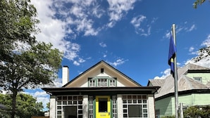 Une maison à deux étages avec une porte jaune, des bordures vertes et un ciel d’un bleu limpide.