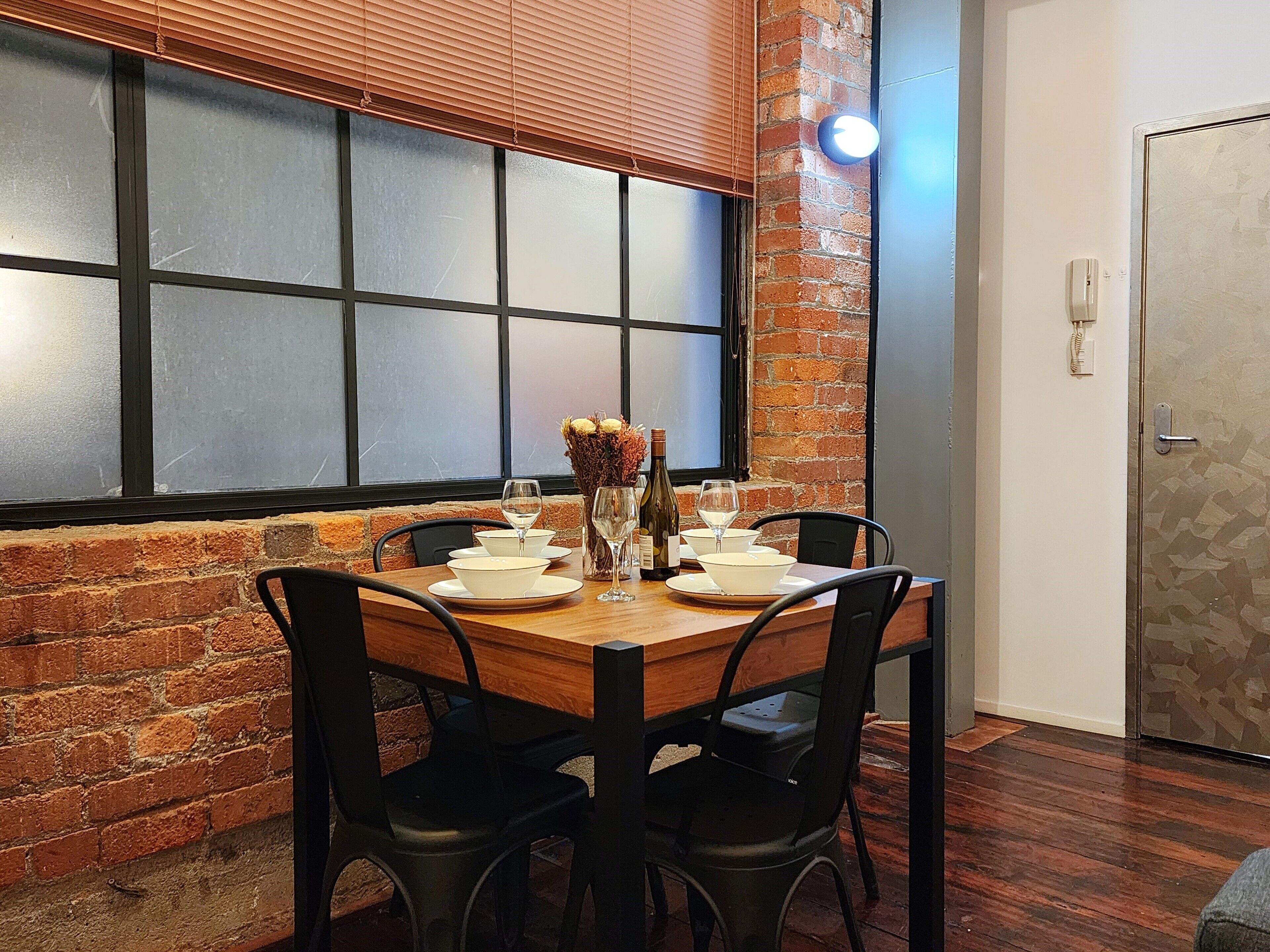 A dining area with a brick wall, a large window with blinds, and a door with a textured wall.