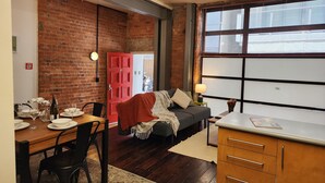 Ein gemütliches Wohnzimmer mit Backsteinwand, einer roten Tür und einem großen Fenster mit Jalousien.