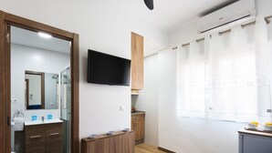 A modern, compact room with a wooden cabinet, a flat-screen TV, a small kitchenette, and a window with curtains. - Cozy Apartment on the Beach, ideal for couples (FUENGIROLA)