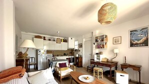 A cozy, well-lit living room with a sofa, wooden coffee table, and a dining area with a table and chairs. A kitchen with white cabinets and a microwave is visible in the background. - Apartment for 4 guests, pet-friendly, 5 minutes from Almanarre Beach – Hyères (HYERES)