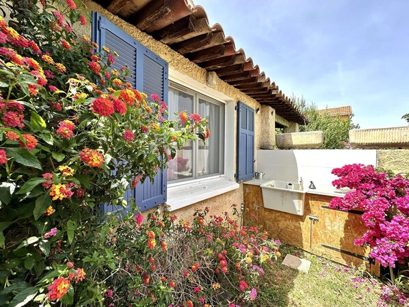 A rustic house with a wooden exterior, a window with blue shutters, and a white outdoor sink.