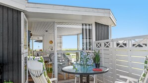 Une terrasse extérieure couverte, avec une table ronde et deux chaises blanches dotées de coussins verts.