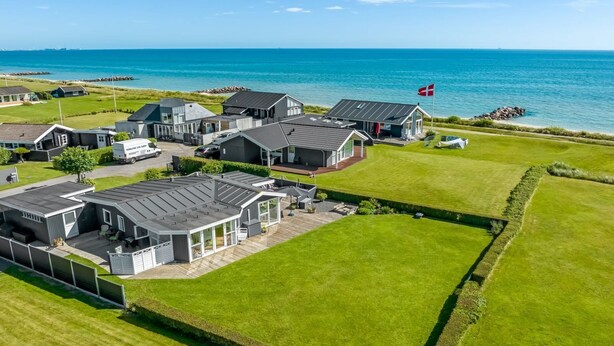 Un quartier résidentiel en bord de mer, avec des maisons modernes, un drapeau et une vue dégagée sur la mer.