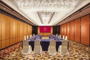 A conference room with a long table, chairs, a chandelier, and a red screen displaying text.
