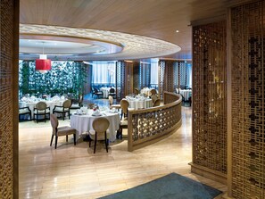 A restaurant with round tables, chairs, and a curved wooden partition. - Grand Millennium Shanghai Hongqiao (Shanghai)
