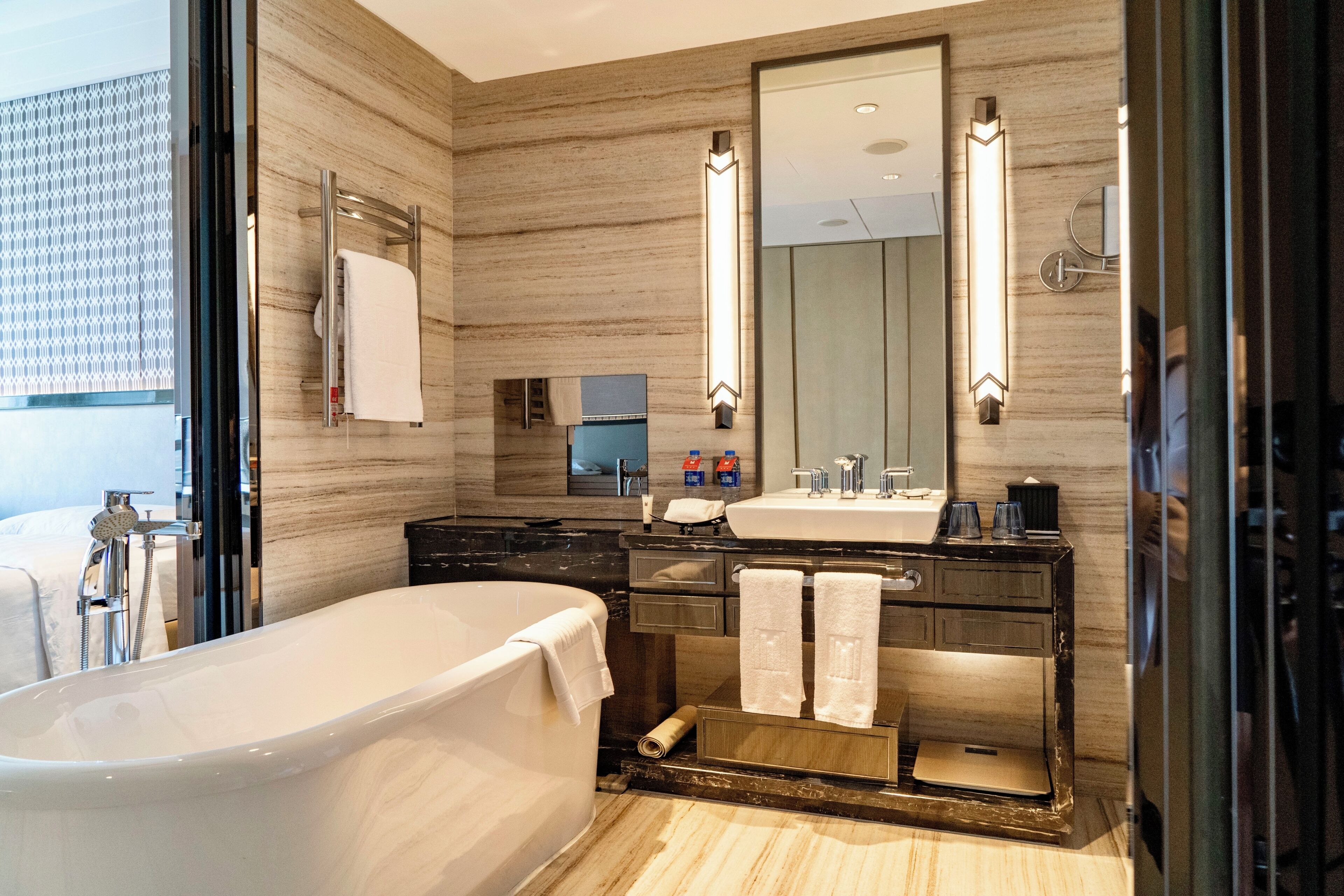 A modern bathroom with a freestanding bathtub, a large mirror, and a vanity with a sink and towel rack.