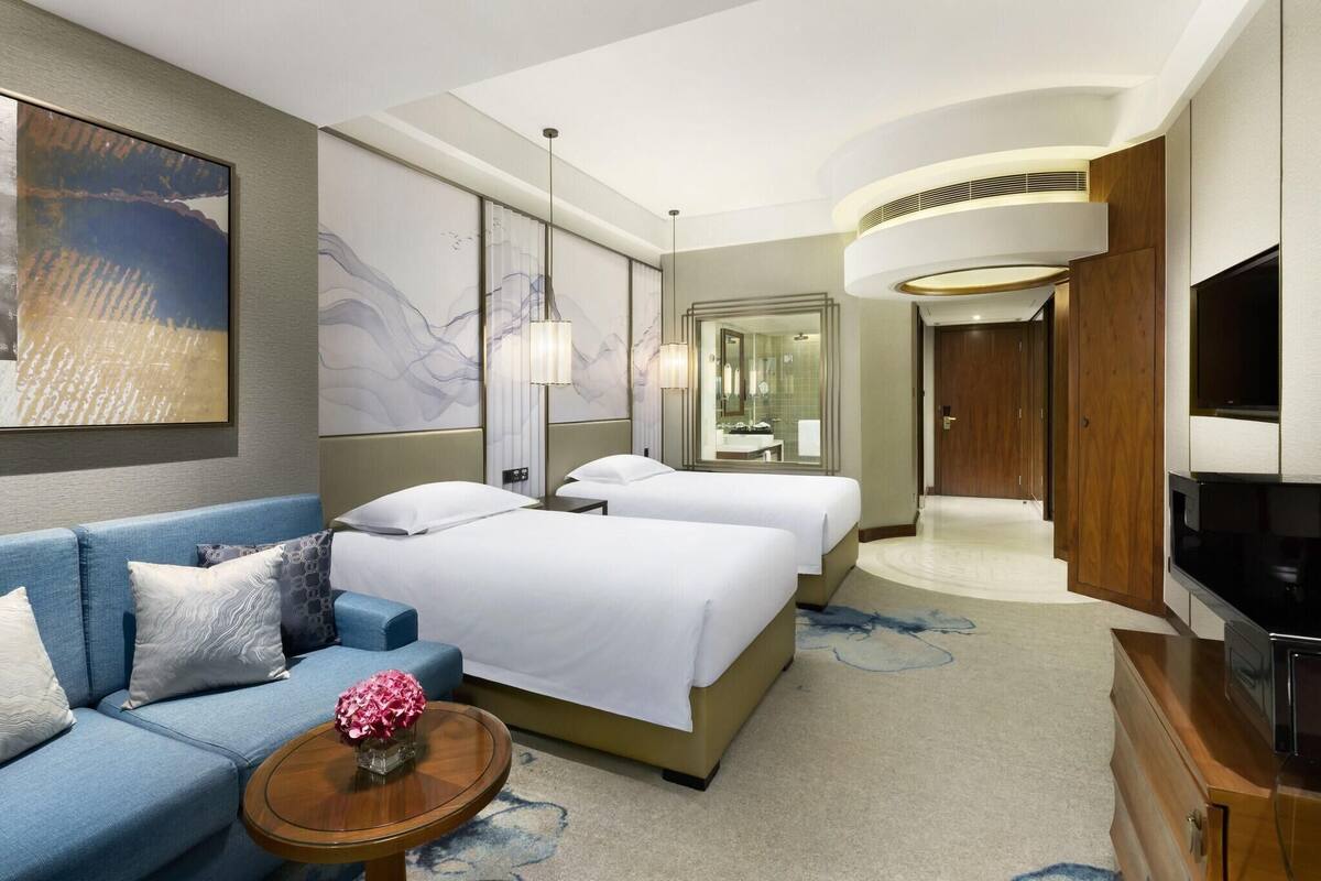 Une chambre d’hôtel avec un canapé, deux lits, une télévision, un miroir et des œuvres d’art accrochées aux murs.
