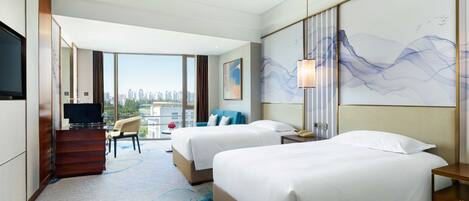 A hotel room with two beds, a TV, a desk, and a large window with a city view.