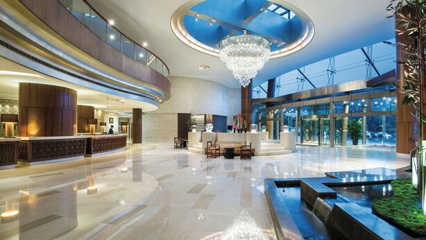 Eine geräumige Lobby mit hoher Decke, einem zentralen Kronleuchter und einer Rezeption.