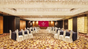 A conference room with a large screen, rows of tables with white chairs, and a patterned carpet. - Grand Millennium Shanghai Hongqiao (Shanghai)