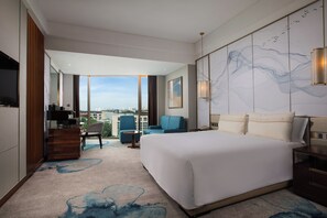 Ein modernes Hotelzimmer mit einem großen Bett, einem Schreibtisch, einem Sessel und Blick auf die Stadt.