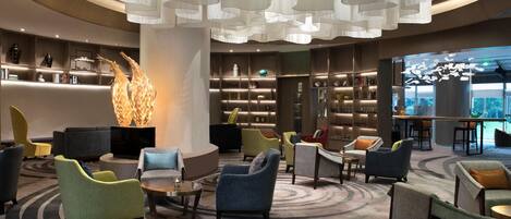 A modern lobby with a central seating area, bookshelves, and a large decorative sculpture.