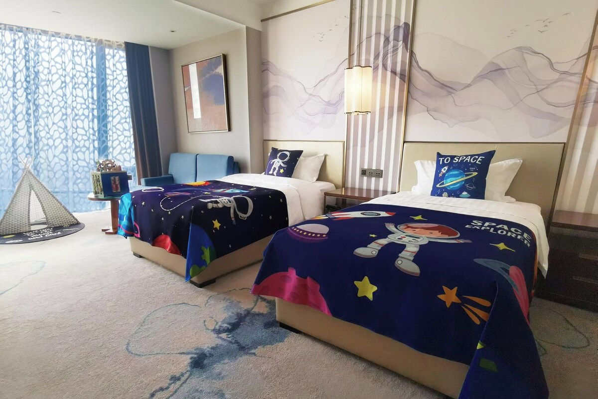 Habitación de hotel con dos camas, un ventanal con cortinas, una lámpara de pared y un cuadro.