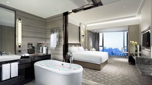 Ein modernes Hotelzimmer mit einer großzügigen Badewanne, einem Bett, einem Badezimmer mit Waschbecken und Spiegel sowie Blick auf die Stadt.