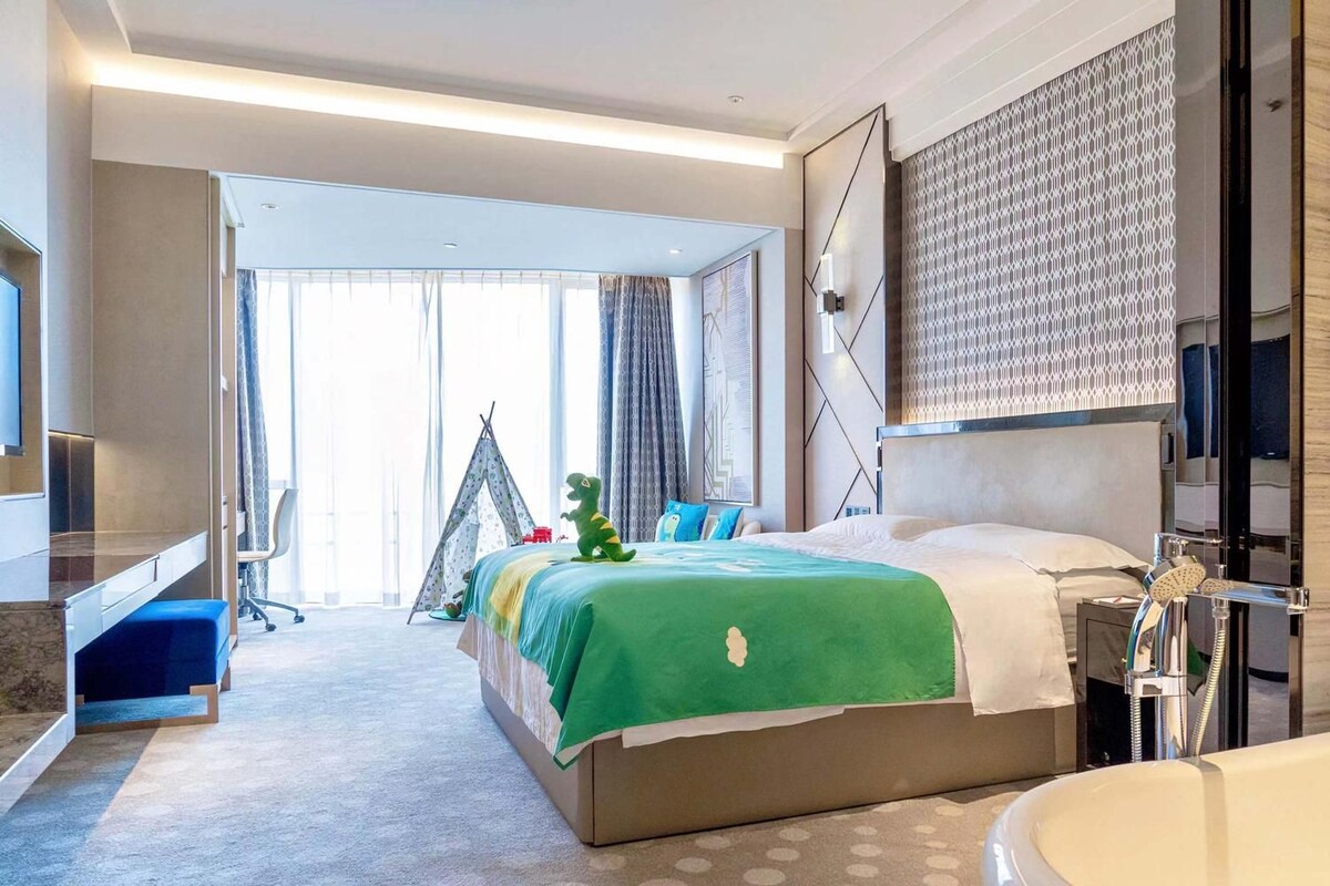 Una habitación de hotel con cama, baño, escritorio y un ventanal grande.
