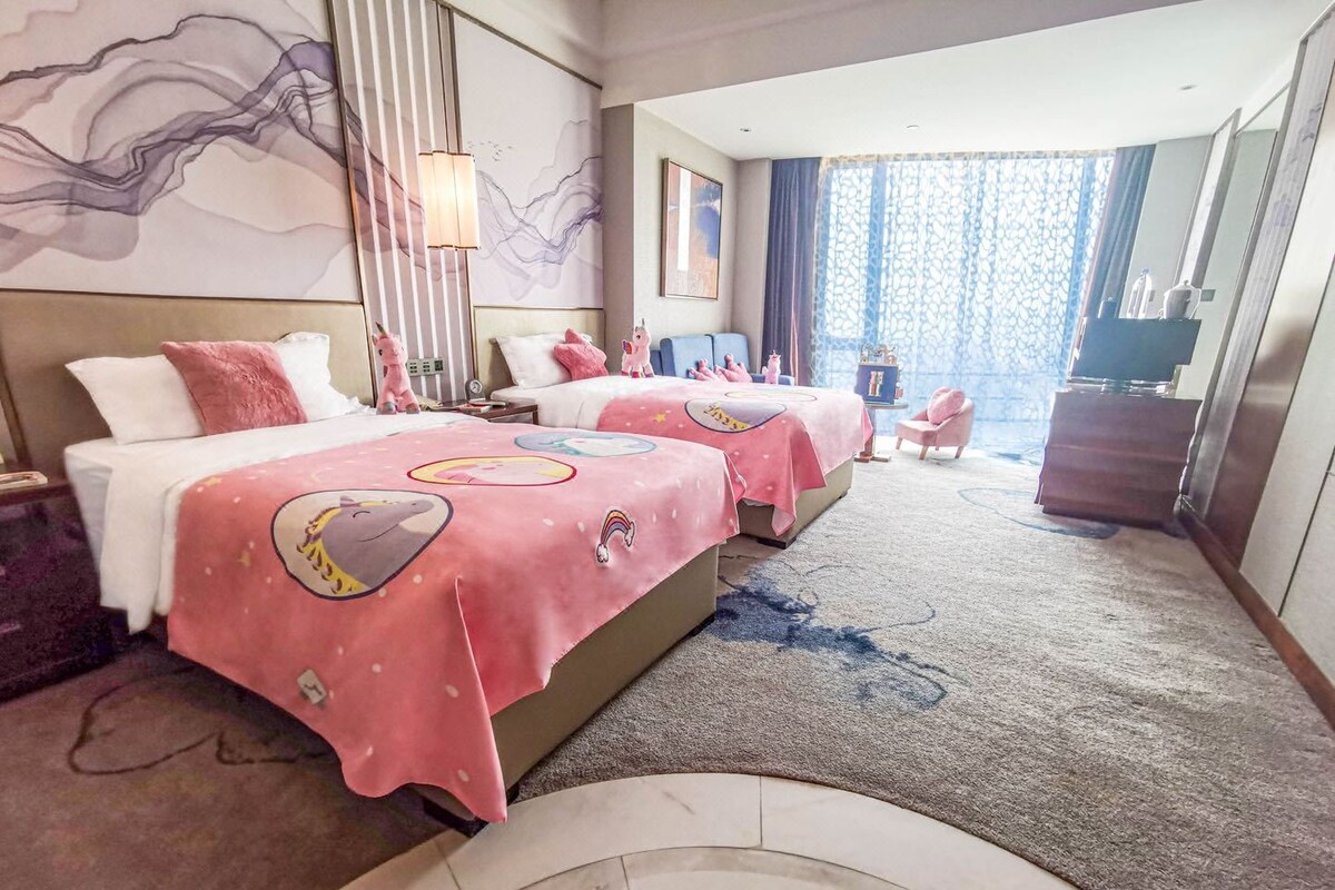 Habitación de hotel con dos camas, un ventanal con vistas, un escritorio y una silla.
