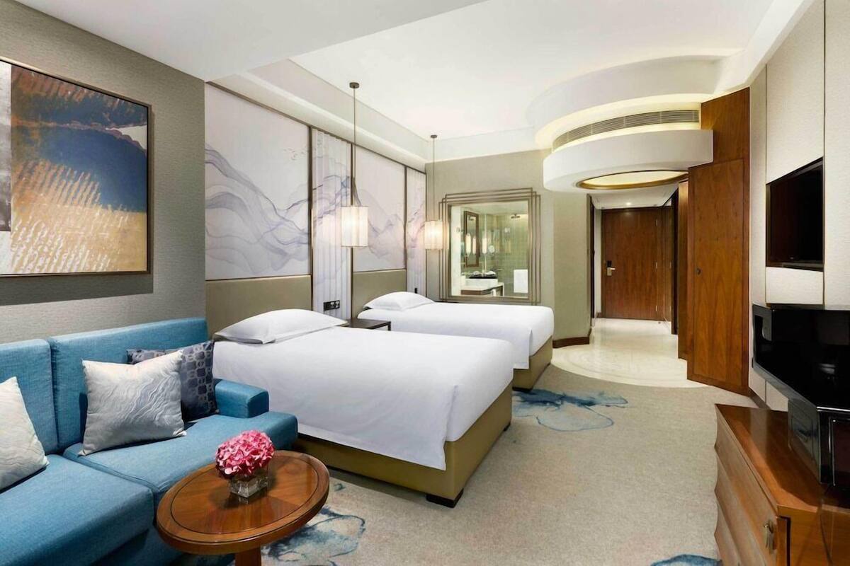 Une chambre d’hôtel avec un canapé, deux lits, une télévision, un miroir et des œuvres d’art accrochées aux murs.