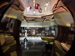 A modern restaurant interior with a central bar, seating area, and a kitchen in the background. - Grand Millennium Shanghai Hongqiao (Shanghai)