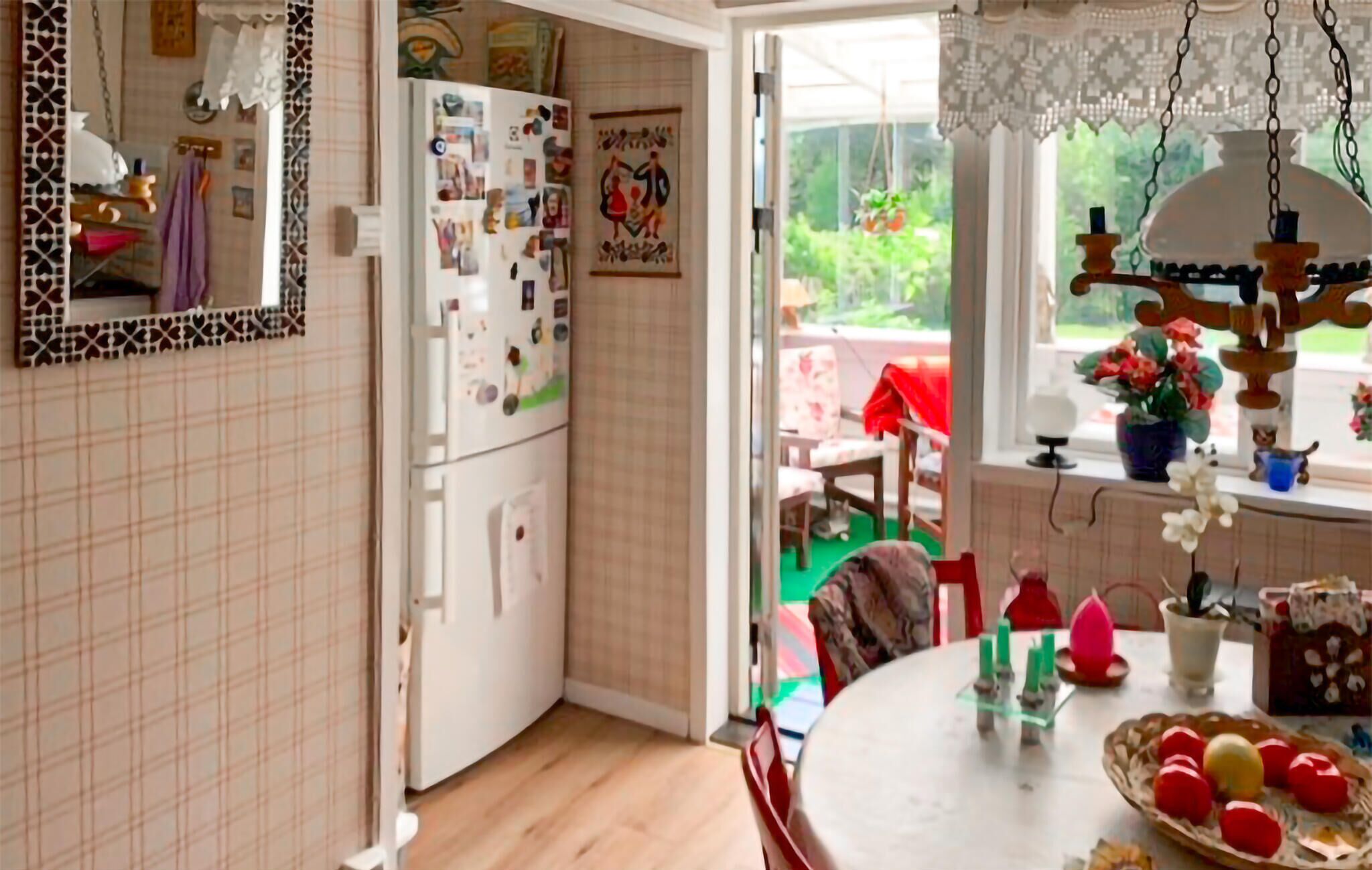 A kitchen with a refrigerator covered in photos, a dining table with a floral centerpiece, and a window with a view of greenery.