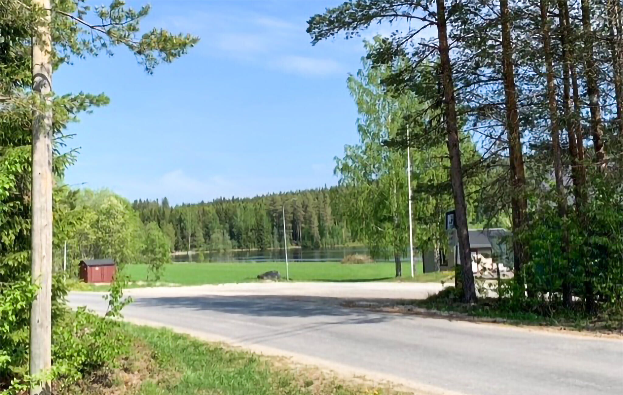 A rural road with a house on the right and a forested area in the background.