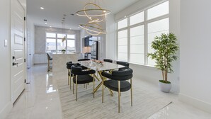 Un espace repas moderne avec une table en marbre, des chaises à revêtement noir et un luminaire suspendu.