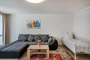 A modern living room with a sofa, a daybed, a small table, and a colorful abstract painting on the wall.