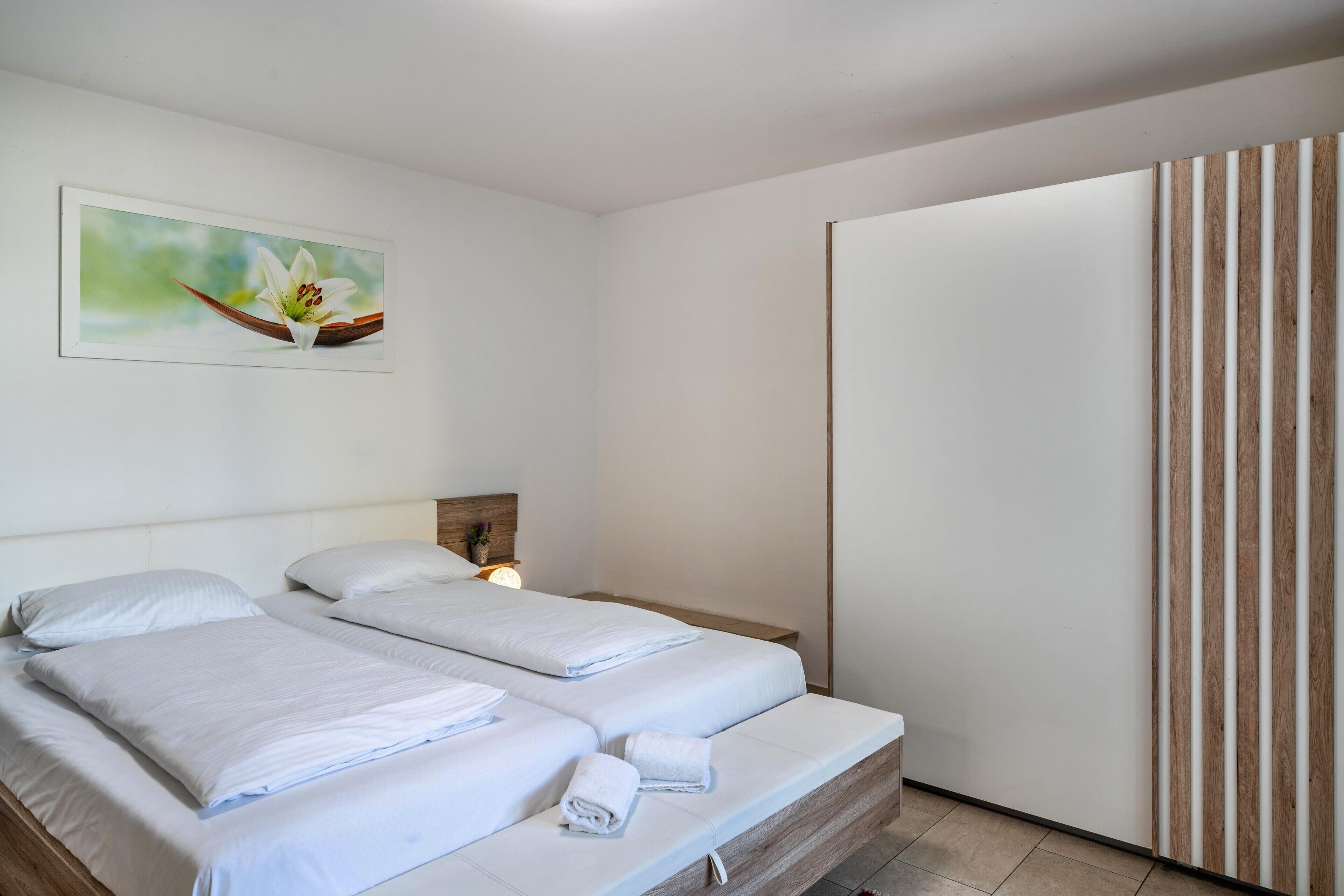A hotel room with two beds, a wooden headboard, a nightstand, a wall-mounted painting, and a wooden panel wall.