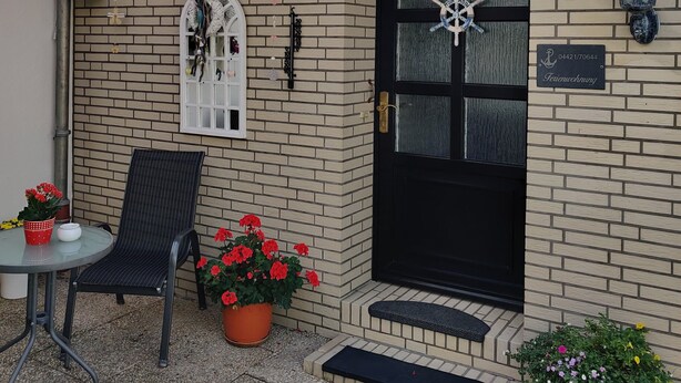 A covered patio area with a wooden ceiling, a black door, and a small step leading to the entrance.
