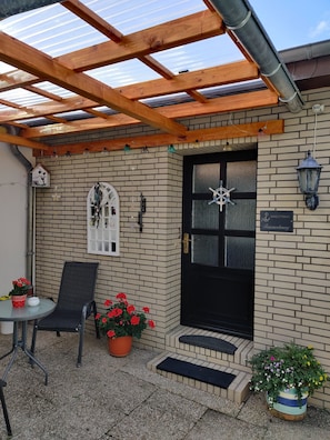 A covered patio area with a wooden ceiling, a black door, and a small step leading to the entrance.