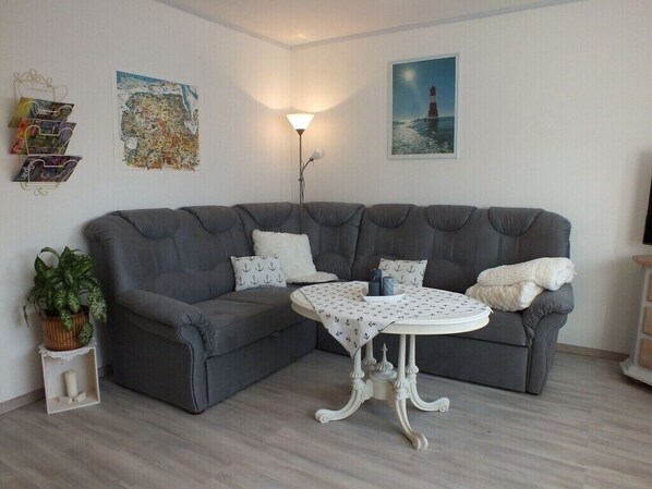 A grey sectional sofa with a small round table in front, a potted plant, and wall art including a lighthouse picture.