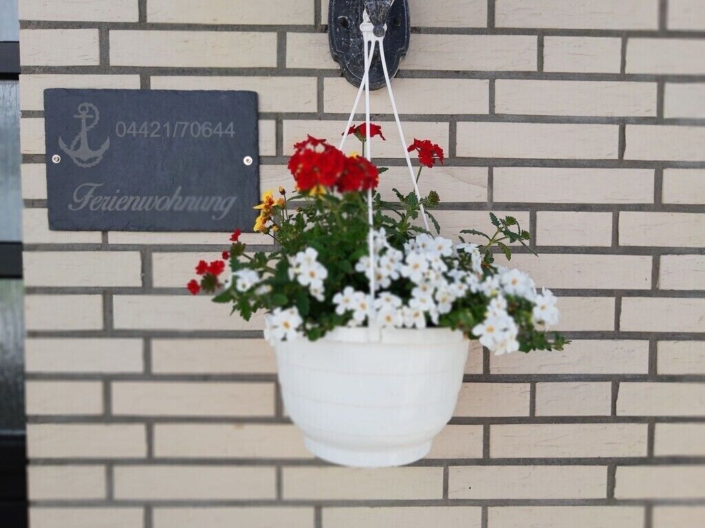 Un vaso da parete bianco con fiori rossi e bianchi, un cartello con un numero e un piccolo oggetto nero sopra il muro.