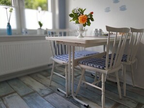A dining area with a table and chairs, a vase with flowers, and a window with blinds.