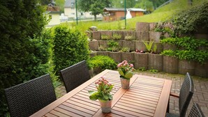 Une table en bois, des chaises, des plantes en pot et un mur de pierre orné de verdure.