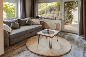 Un salon avec un canapé, une table basse, un radiateur et une vue sur la verdure à l’extérieur.