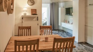 Un coin repas avec une table et des chaises en bois, une horloge au mur et une vue sur la cuisine.