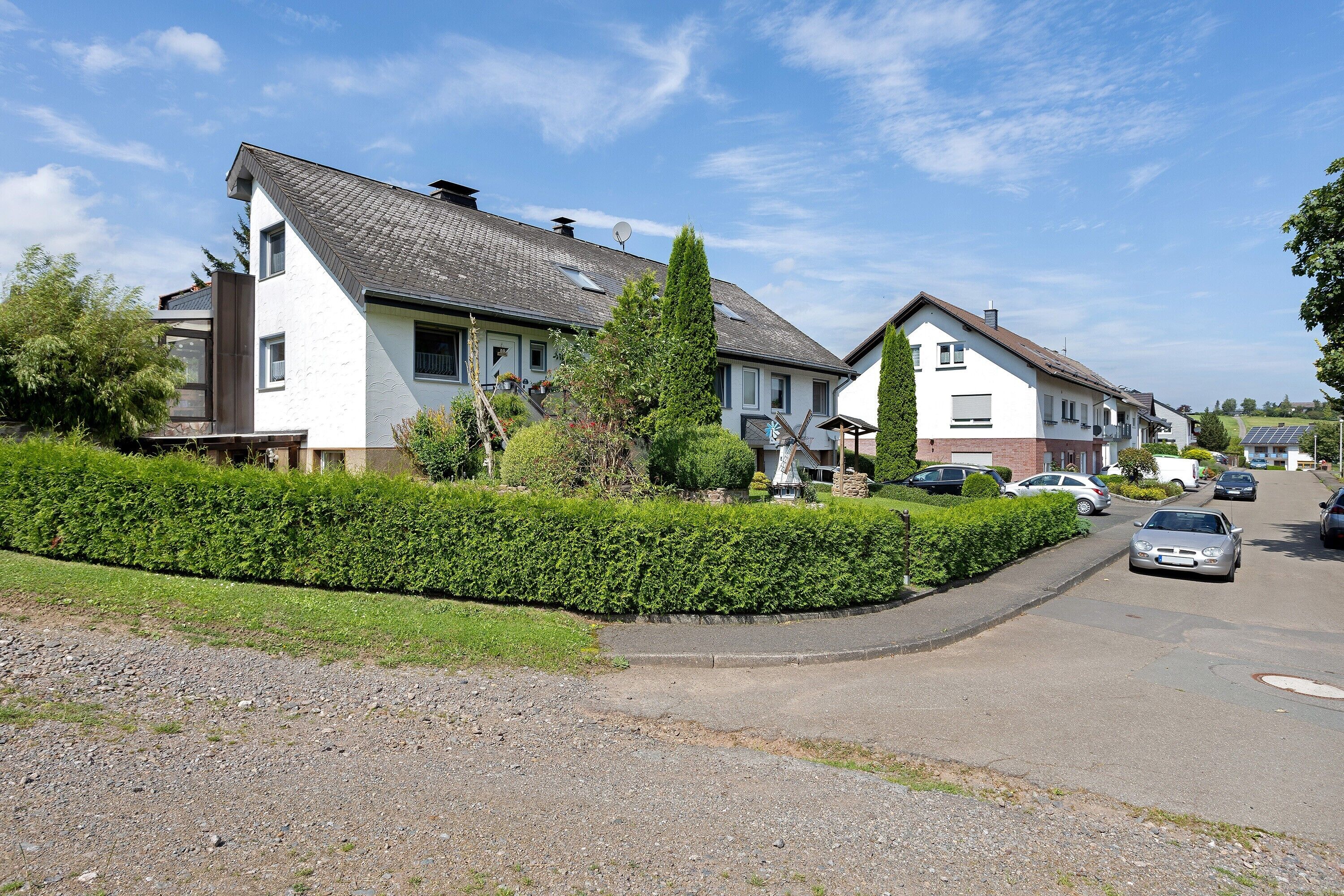 Eine Wohnstraße mit Häusern, einer Hecke und einem Schotterweg.