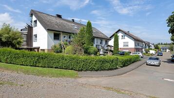 Eine Wohnstraße mit Häusern, einer Hecke und einem Schotterweg.