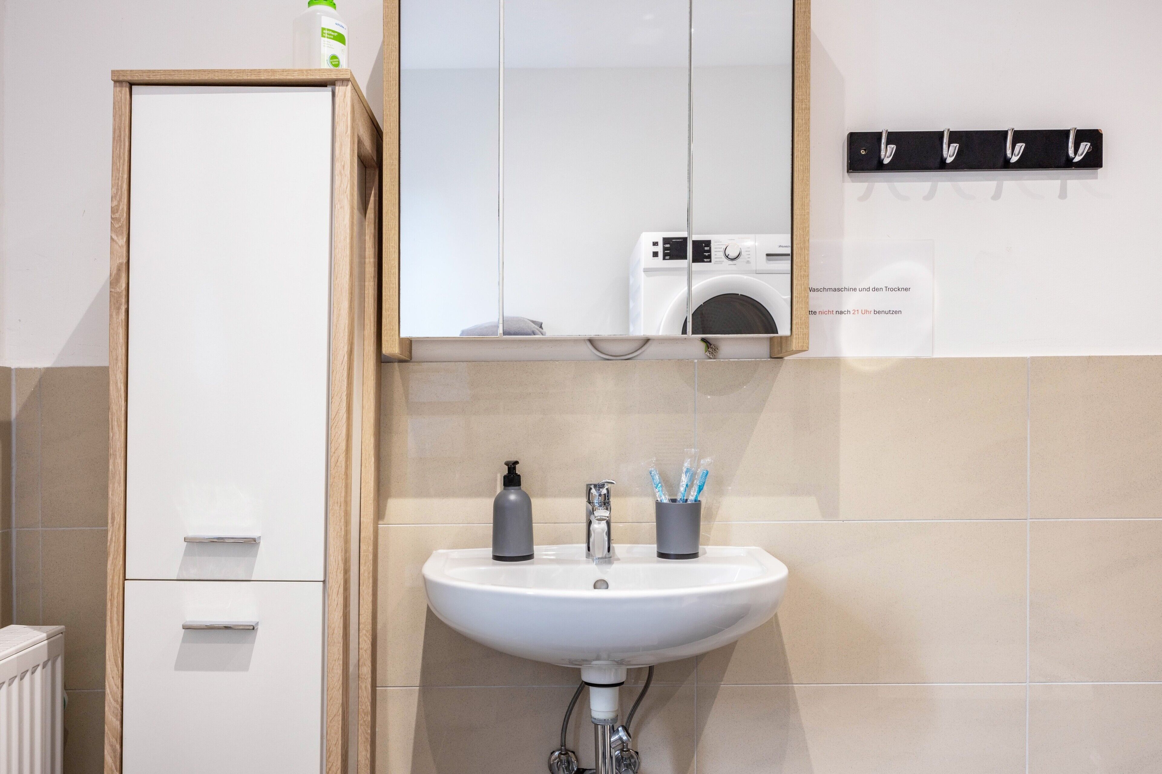 A bathroom with a white sink, a mirror, a washing machine, and a towel rack.