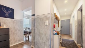 Un couloir avec un mur gris à texture, un plancher en bois, un tableau électrique blanc et un jouet rouge posé sur une étagère.