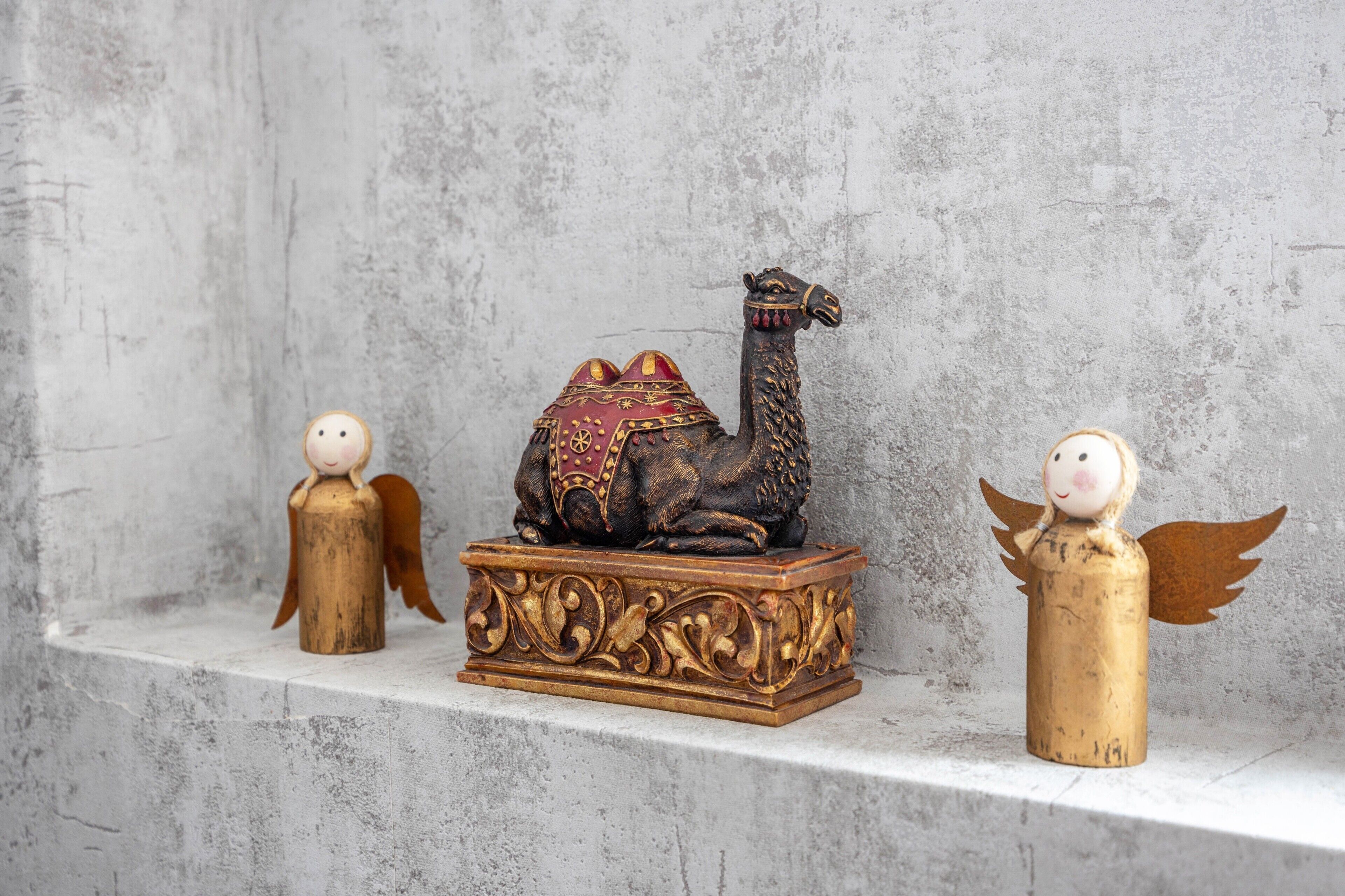 En skulptur av en kamel, placerad på en piedestal, med två små änglafigurer på vardera sidan.
