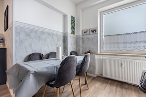 En matplats med ett bord dukat för fyra personer, ett element, ett fönster med utsikt och en vägg med inramade tavlor.