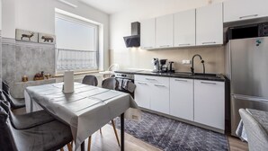 Une cuisine moderne avec des meubles blancs, un réfrigérateur en acier inoxydable et un coin repas comprenant une table et des chaises.