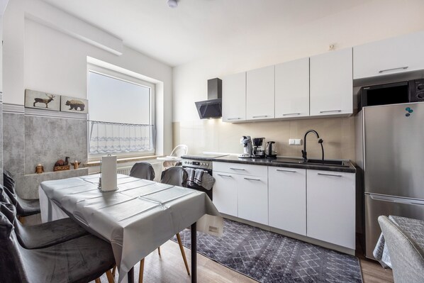 A modern kitchen with white cabinets, a stainless steel refrigerator, and a dining area with a table and chairs.