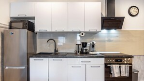 Eine moderne Küche mit Edelstahlgeräten, weißen Schränken, einem eingebauten Backofen und einer Wanduhr.