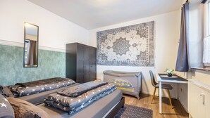 Ein Schlafzimmer mit Bett, Schreibtisch, Stuhl, Heizkörper, Kleiderschrank und Wandteppich.